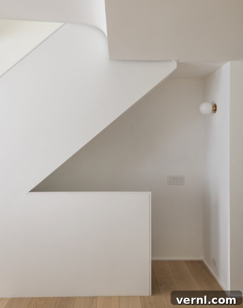 Brooklyn Row House Renovation for Modern Family Living 12
Minimalist hallway with white angular staircase and brass wall sconce.