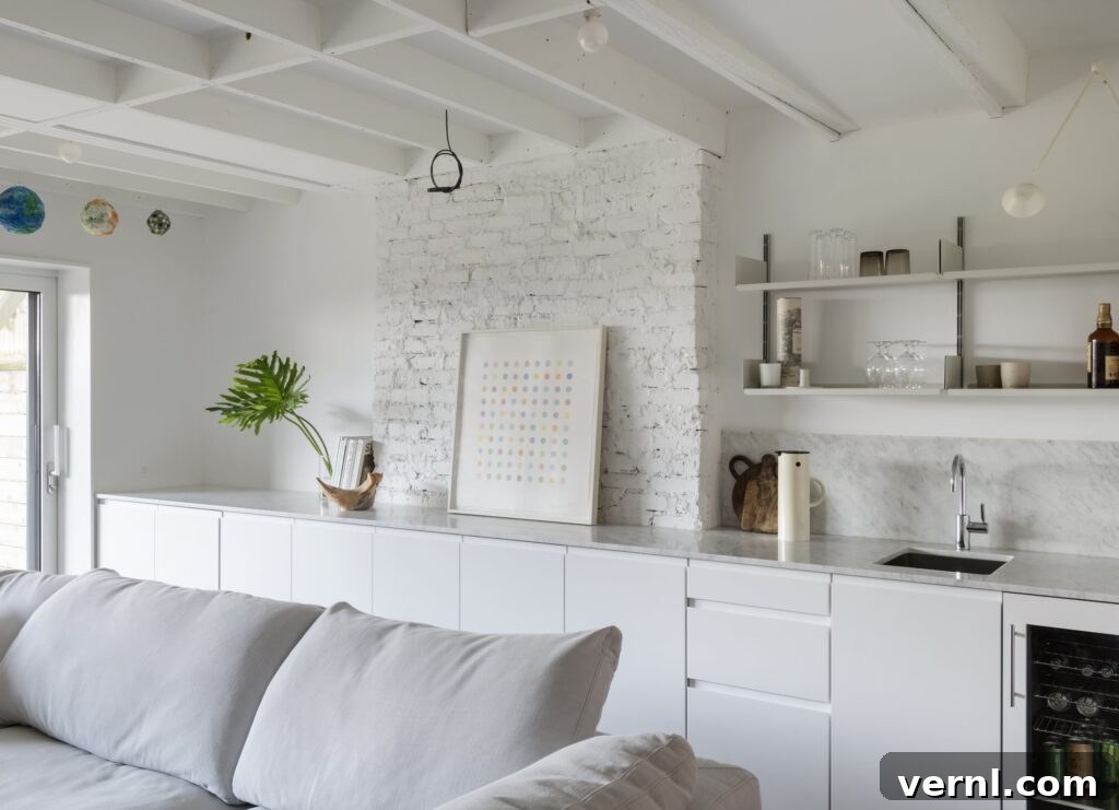 Brooklyn Row House Renovation for Modern Family Living 8
Open-plan kitchen and living area with white cabinetry, exposed beams, and painted brick feature wall.
