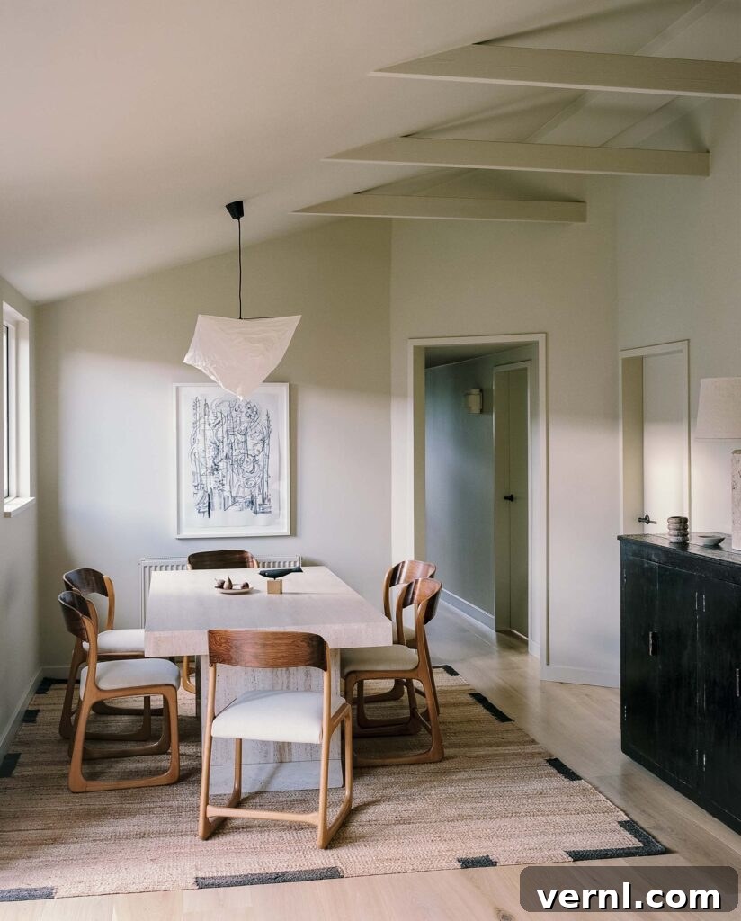 Inside a Dorset Beach House: Modern Coastal Living 11 Travertine dining table with sculptural wooden chairs under exposed rafters.