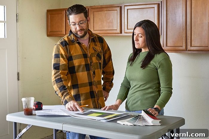 A man and woman stand at a table looking at papers and color samples, appearing to discuss home renovation plans.